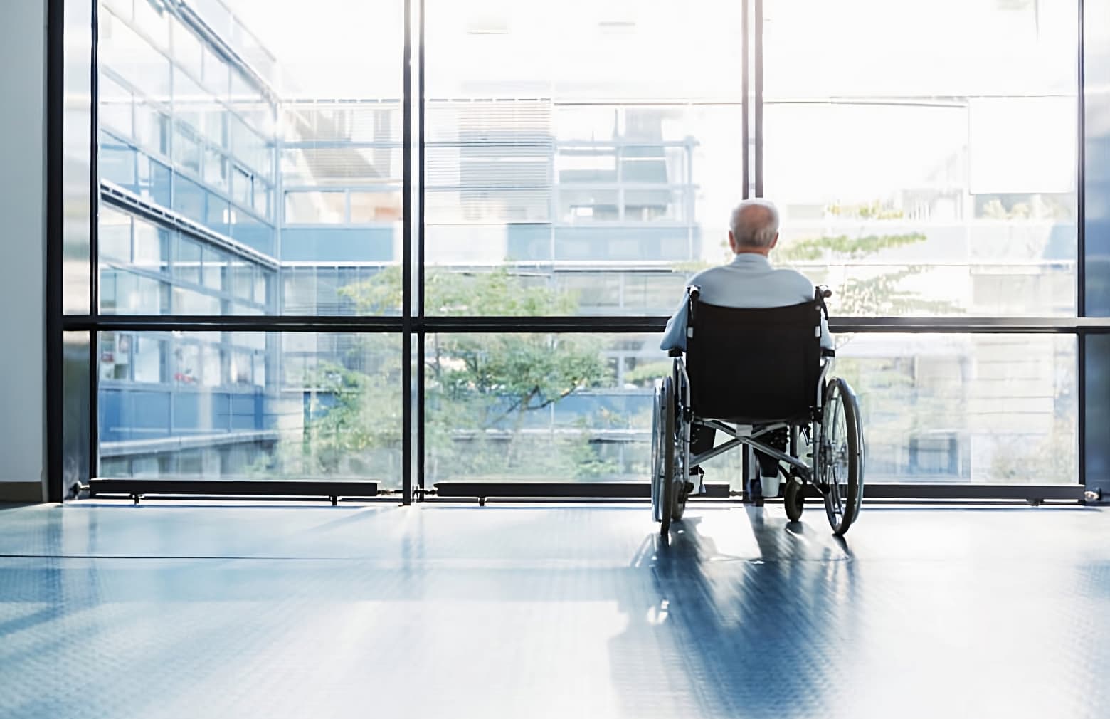 image of old man siting on a wheel chair looking out a glass wall